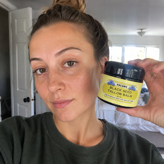 Woman holding Volume Black Seed Tallow Balm 2oz jar next to her bare face